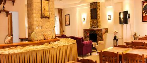 Una habitación de hotel acogedora con chimenea, un comedor con mesas y sillas de madera, y una sala de estar con sofá y un espejo grande.