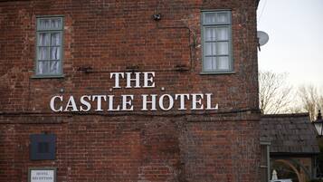 A brick building with a sign that reads "The Castle Hotel." There is a sign indicating the hotel reception and a satellite dish on the roof.