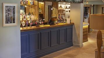 A bar area with a wooden counter, various bottles, and a framed artwork on the wall.