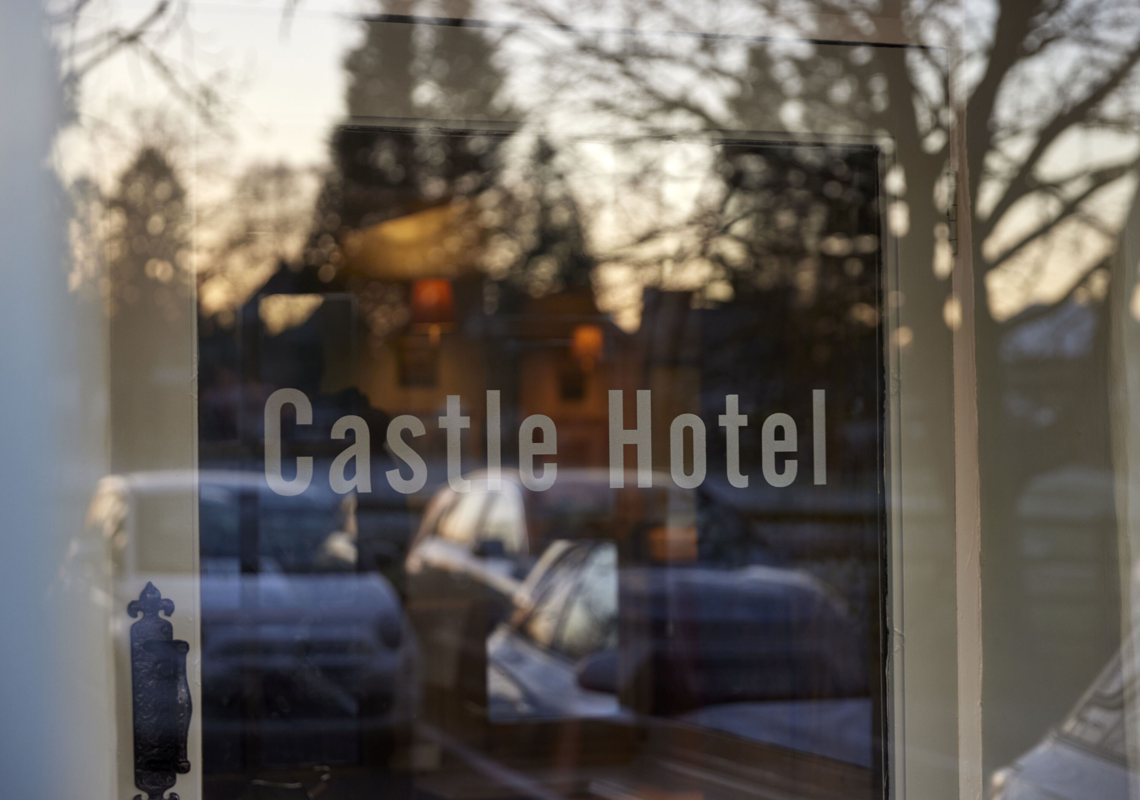 Ein Fenster mit dem Schriftzug "Castle Hotel" und Spiegelungen von parkenden Autos und Bäumen.