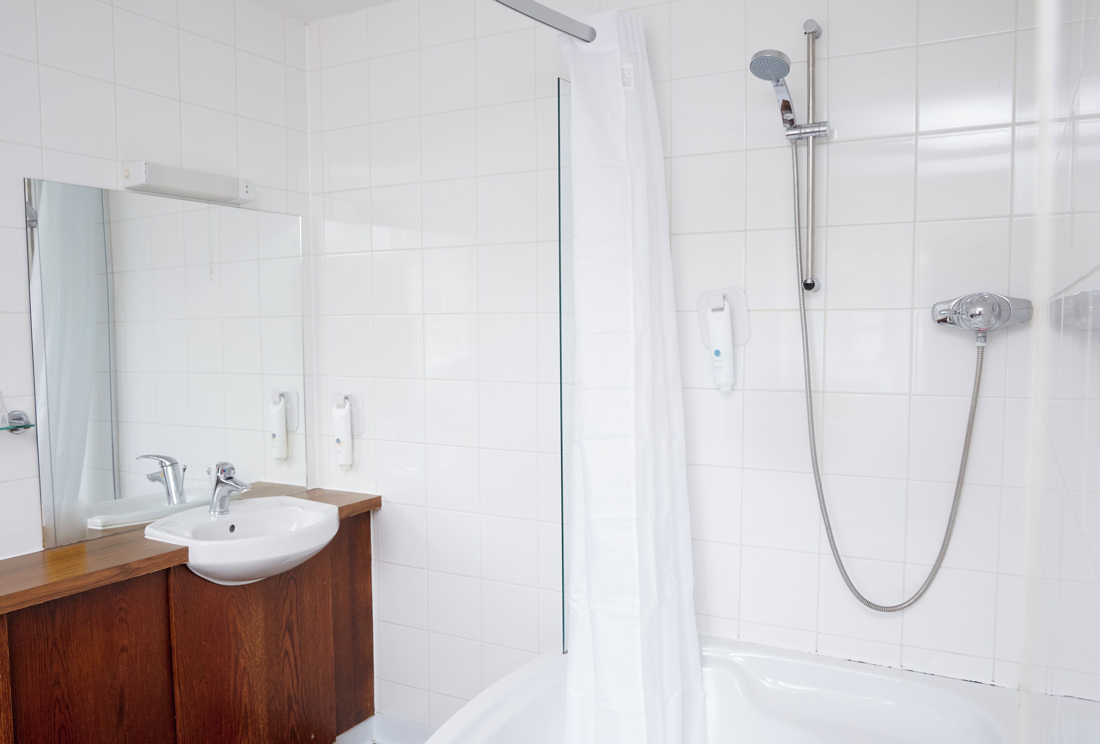 A modern bathroom with a white sink, wooden vanity, a large mirror, and a shower with a glass door.