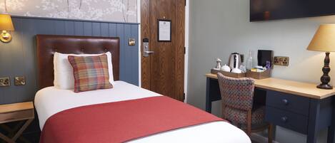 A hotel room with a bed, a desk, a chair, a TV, and a door.