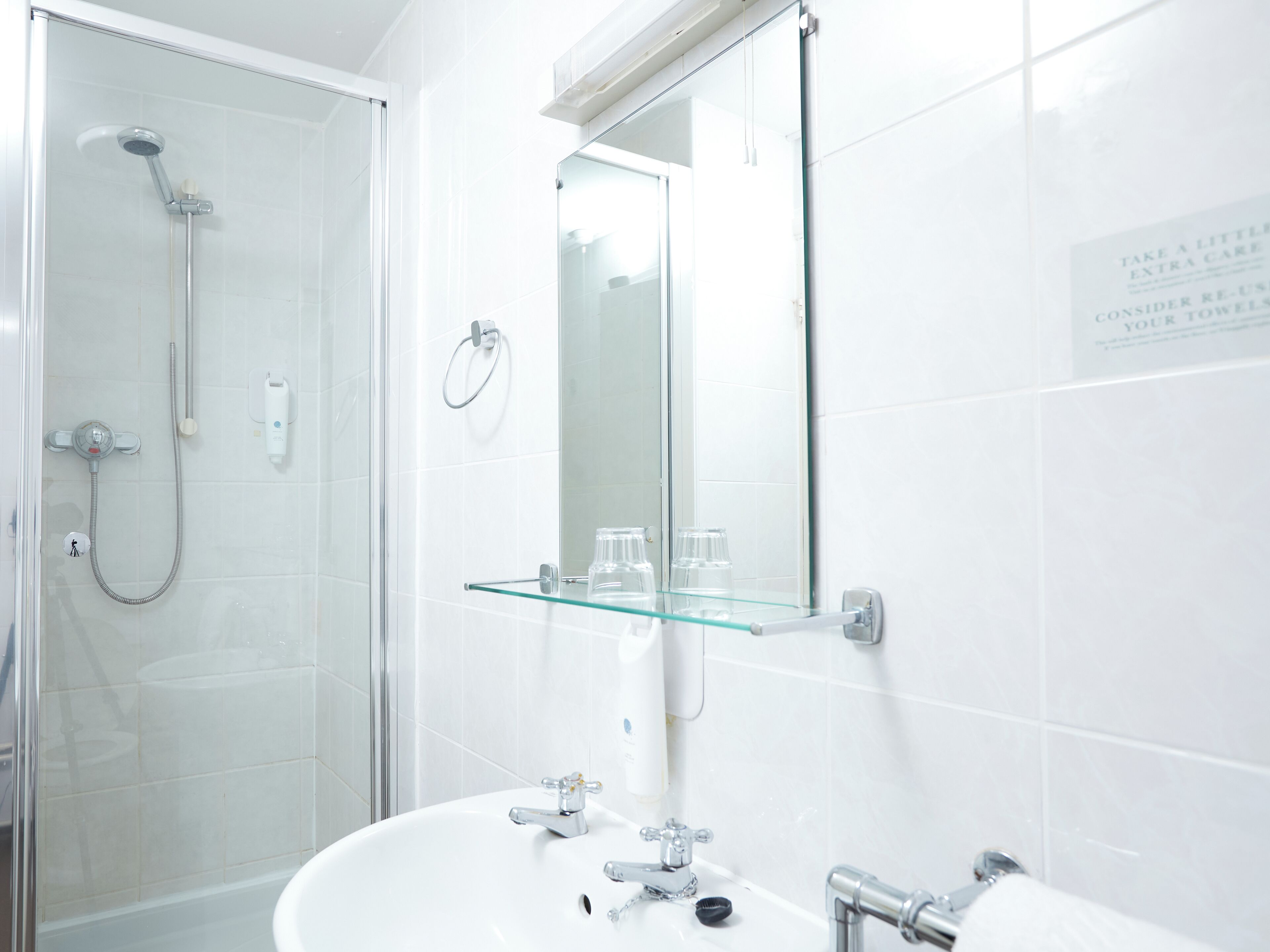 A modern bathroom with a glass shower enclosure, a white sink with chrome fixtures, and a glass shelf above the mirror.