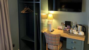A hotel room with a bed, a desk with a lamp, a chair, a wardrobe, and a TV on the wall.