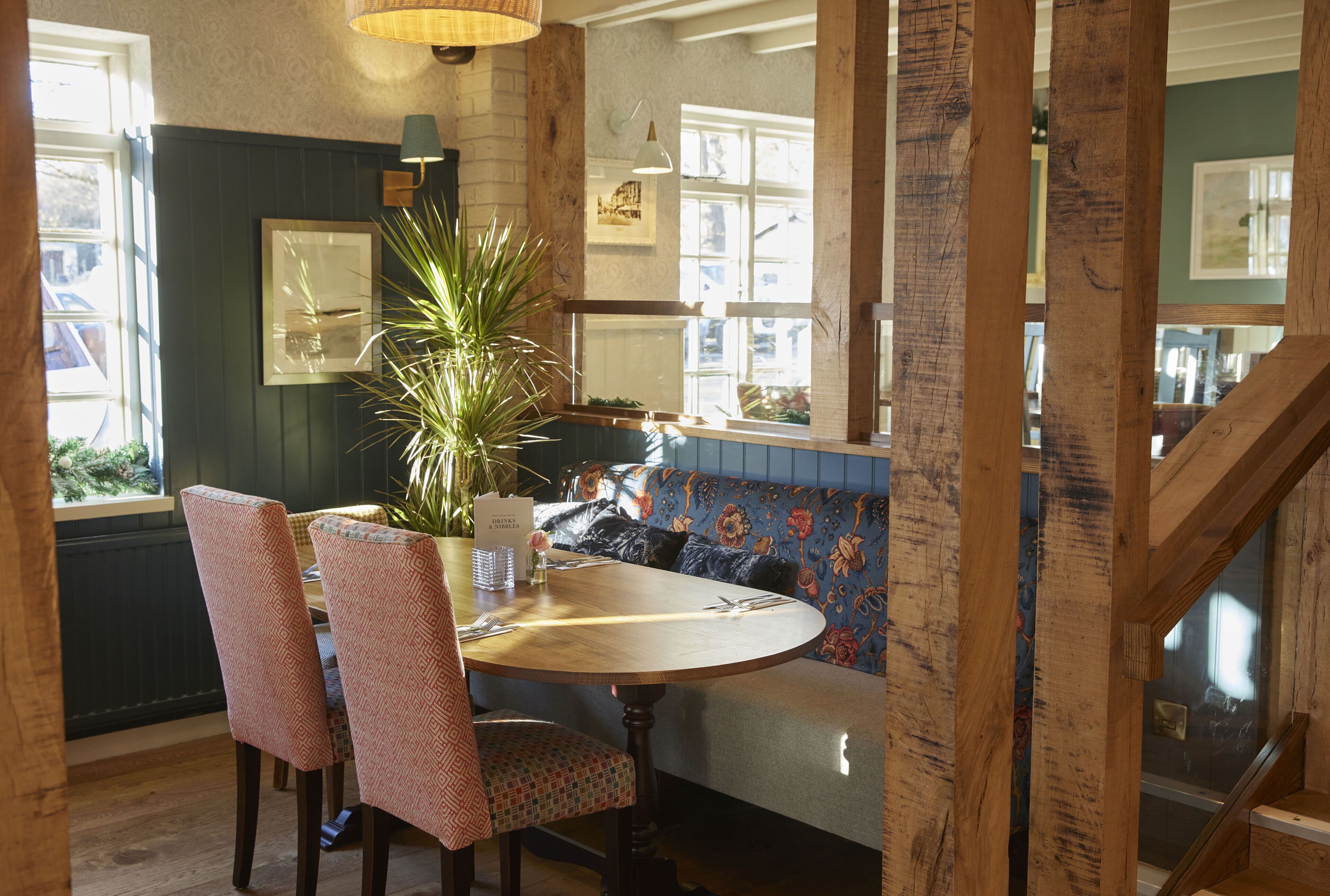 A dining area with a round wooden table, two patterned chairs, a bench with floral upholstery, and a potted plant.