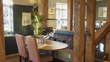 A dining area with a round wooden table, two patterned chairs, a bench with floral upholstery, and a potted plant.