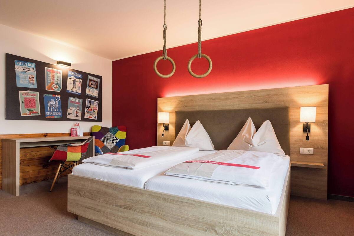 Ein Hotelzimmer mit einem hölzernen Bett, zwei Nachttischlampen, einem Schreibtisch mit Stuhl und einer Wand mit Postern.