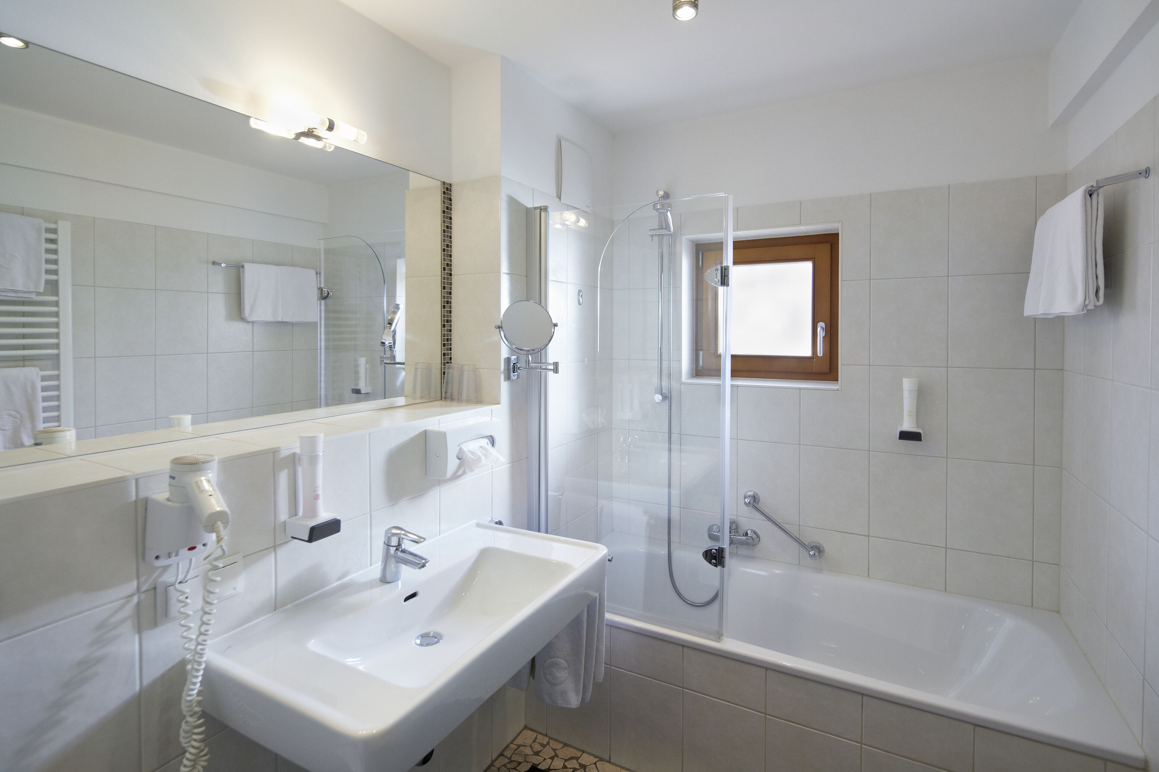 Un baño moderno con un lavamanos blanco, una ducha con mampara de cristal y un espejo grande.