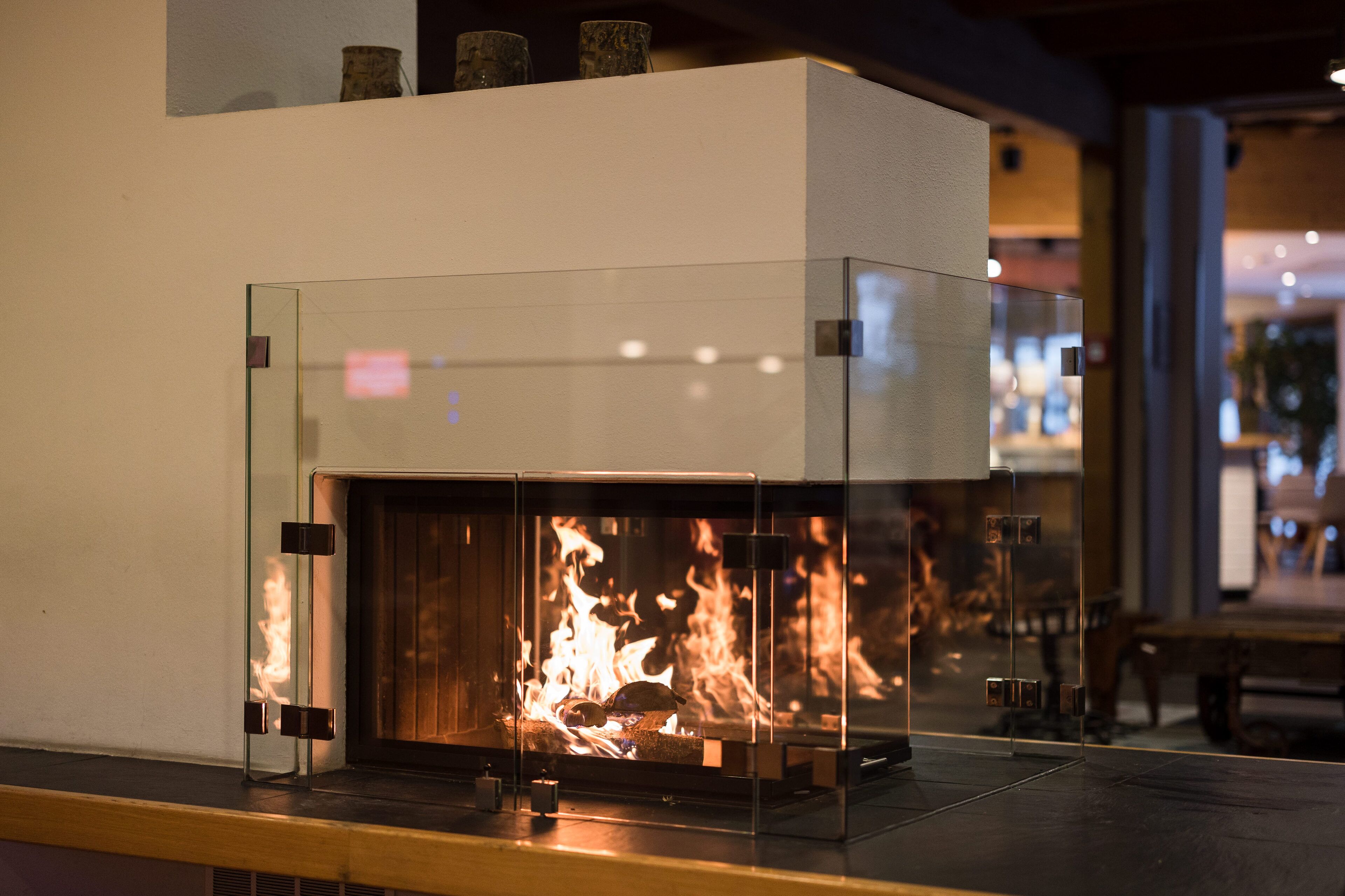 A modern fireplace with a glass enclosure, visible flames, and a wooden mantel.