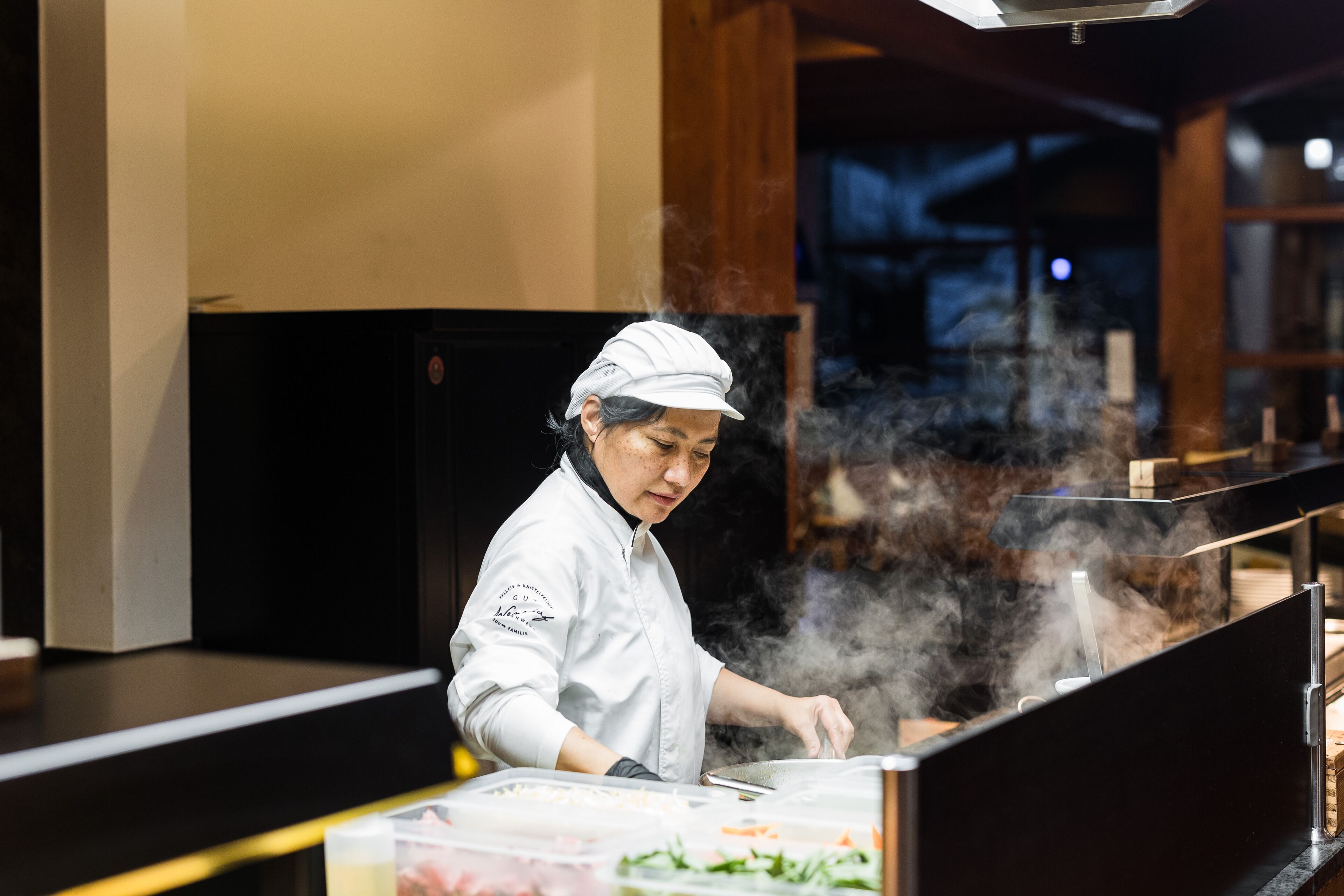 Un chef trabajando en una barra, con vapor ascendiendo, rodeado de utensilios de cocina e ingredientes.