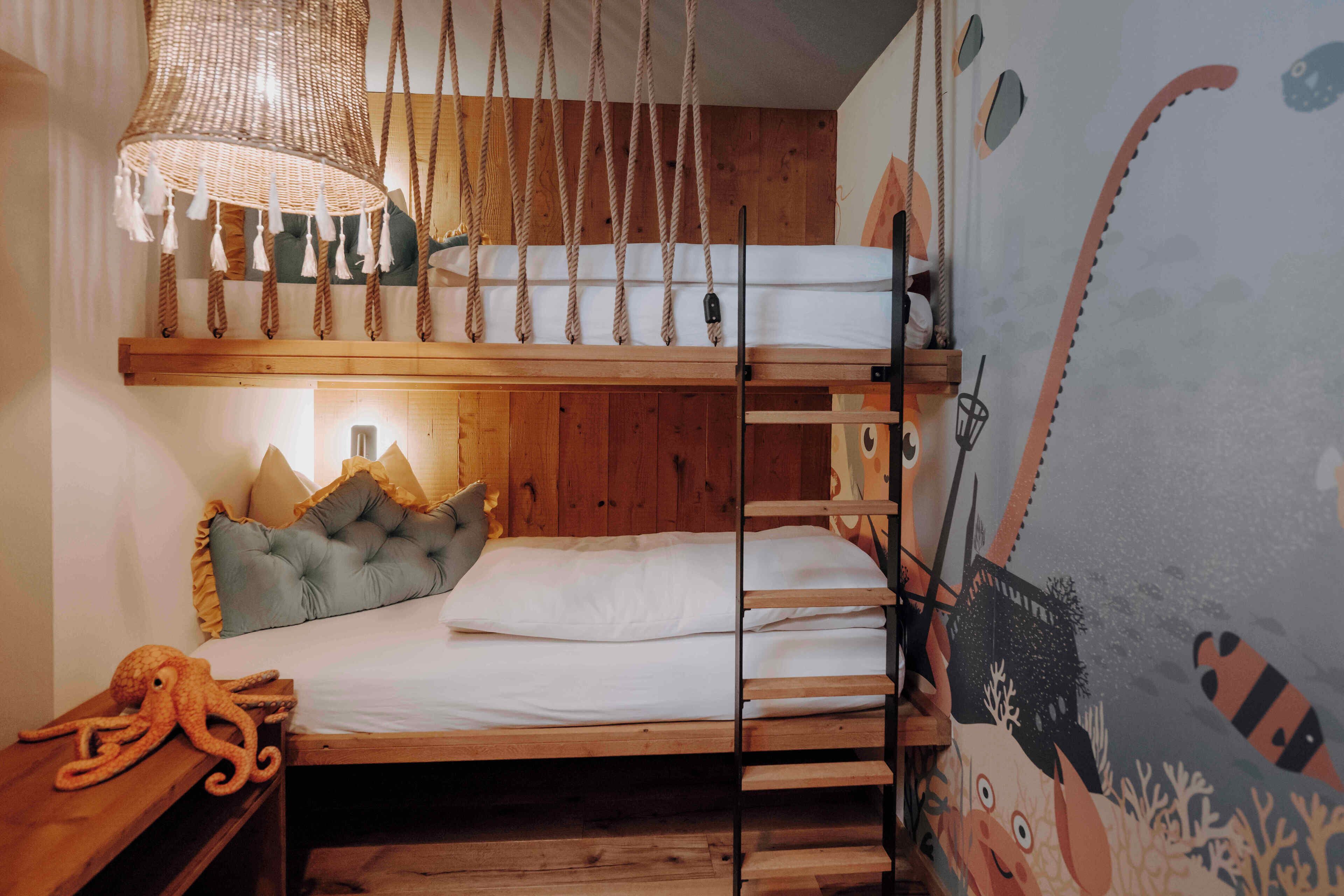 A bunk bed with a wooden headboard, a hanging chair, and a wall mural.