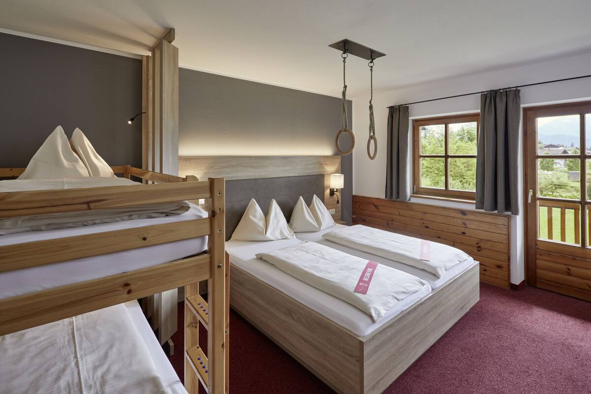 Ein Zimmer mit zwei Etagenbetten, einem großen Fenster mit Vorhängen und Blick auf Grünflächen.