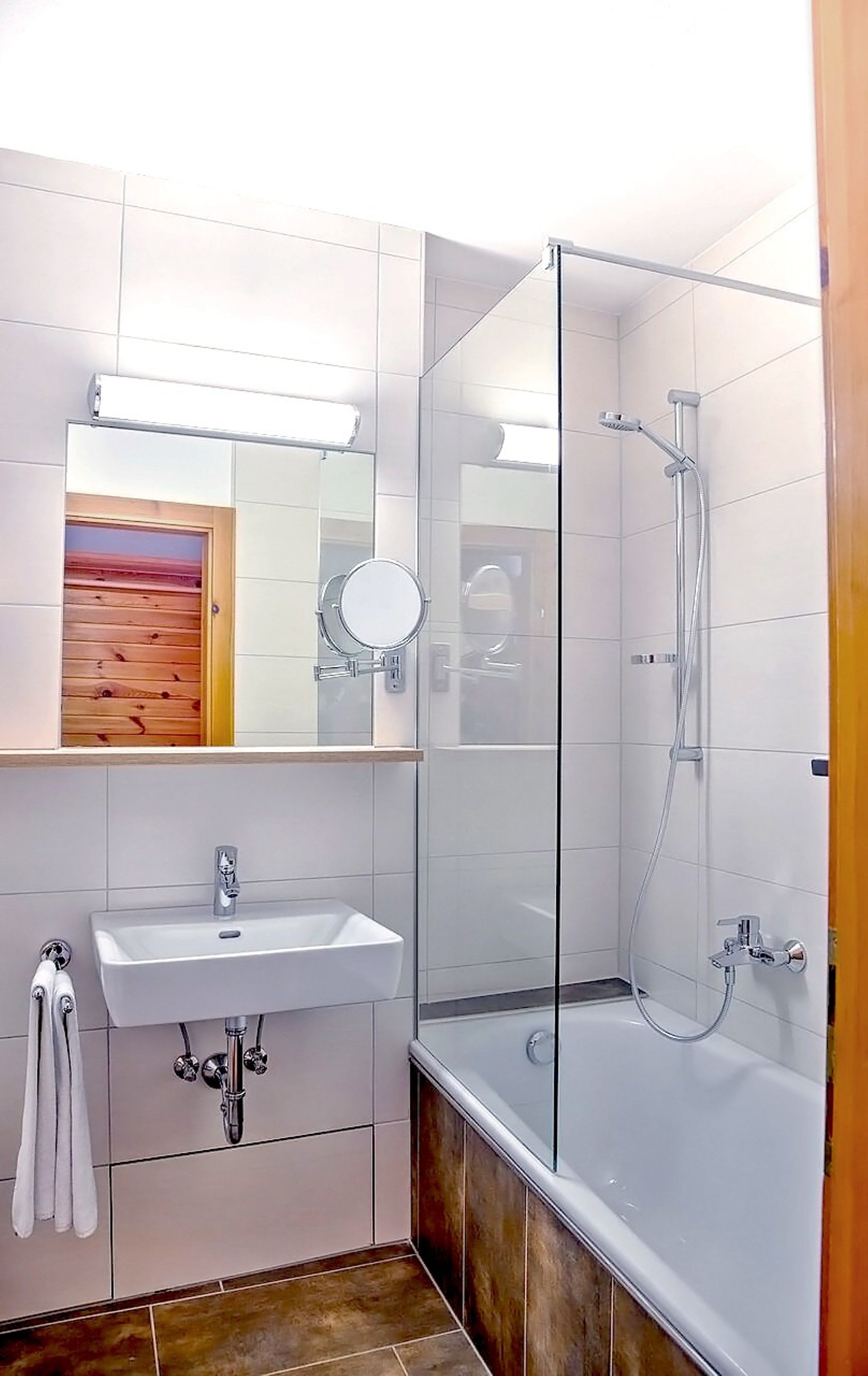 Ein modernes Badezimmer mit einer gläsernen Duschkabine, einem Waschbecken mit Spiegel und einer Holztür.