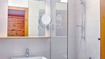 Ein modernes Badezimmer mit einer gläsernen Duschkabine, einem Waschbecken mit Spiegel und einer Holztür.