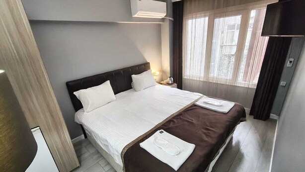 A hotel room with a bed, a nightstand, a lamp, an air conditioning unit, and a window with curtains. - Sun Suites (Istanbul)