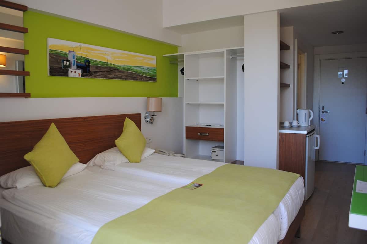 A hotel room with a bed, a desk, a coffee machine, and a painting on the wall.