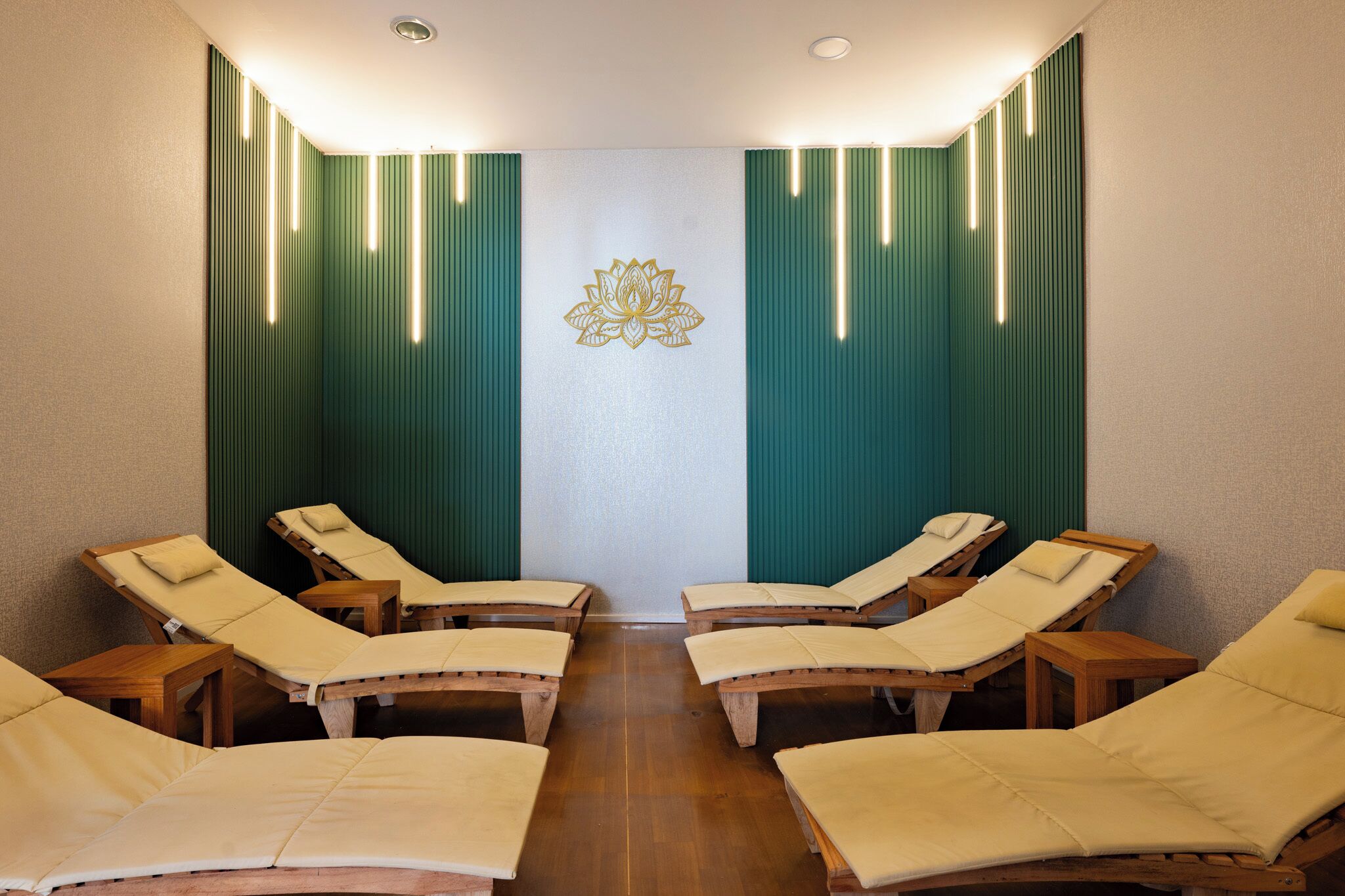 A room with six wooden sun loungers, a central wall with a decorative emblem, and vertical light fixtures.