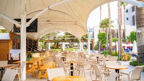 An outdoor café with tables and chairs, a covered seating area, and a view of the surrounding buildings and greenery. - Calimera Side Resort - All inclusive (Manavgat)