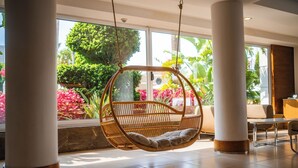 A hanging chair in a spacious room with large windows, a reception desk, and a tiled floor. - Calimera Side Resort - All inclusive (Manavgat)