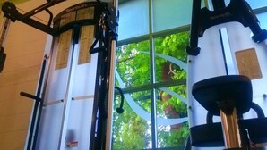 A gym with exercise equipment, including a treadmill and weight machines, with a view of trees through a window. - Fieldways (Trowbridge)