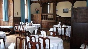 A dining area with round tables covered with white tablecloths, wooden chairs, and a wooden cabinet with a mirror. - Fieldways (Trowbridge)
