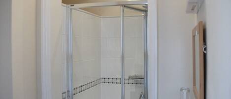 A glass-enclosed shower with a tiled floor and a corner showerhead.