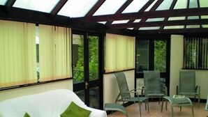 A conservatory with a glass ceiling, a white sofa with green cushions, and several chairs. - Fieldways (Trowbridge)