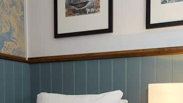 A neatly made bed with white linens, a wooden nightstand with a lamp, and two framed artworks on the wall.