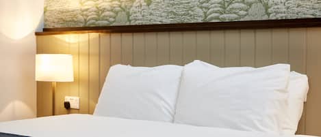 A hotel room with a bed, a wall-mounted lamp, and a floral wallpaper design.