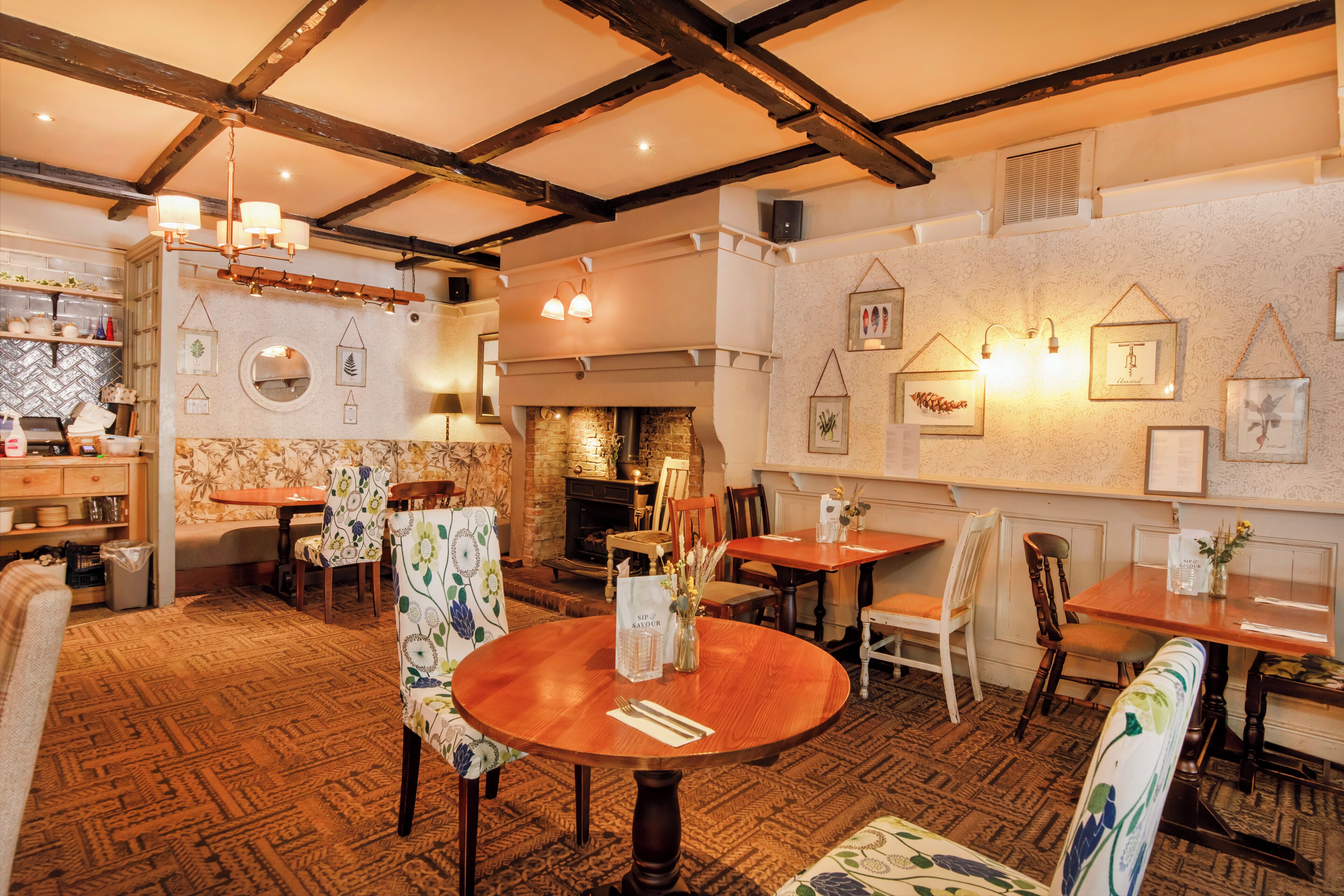 Un restaurante acogedor con mesas y sillas de madera, una chimenea y decoración artística en las paredes.