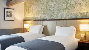 Una habitación de hotel con dos camas, un papel tapiz estampado y un cuadro en la pared.