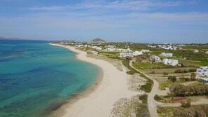 A coastal village with white buildings, a sandy beach, and a mountain in the background.