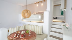 Una habitación moderna y bien iluminada con una mesa de comedor de madera preparada para una comida, una zona de estar acogedora con cojines a rayas, y una escalera que sube a un nivel superior.