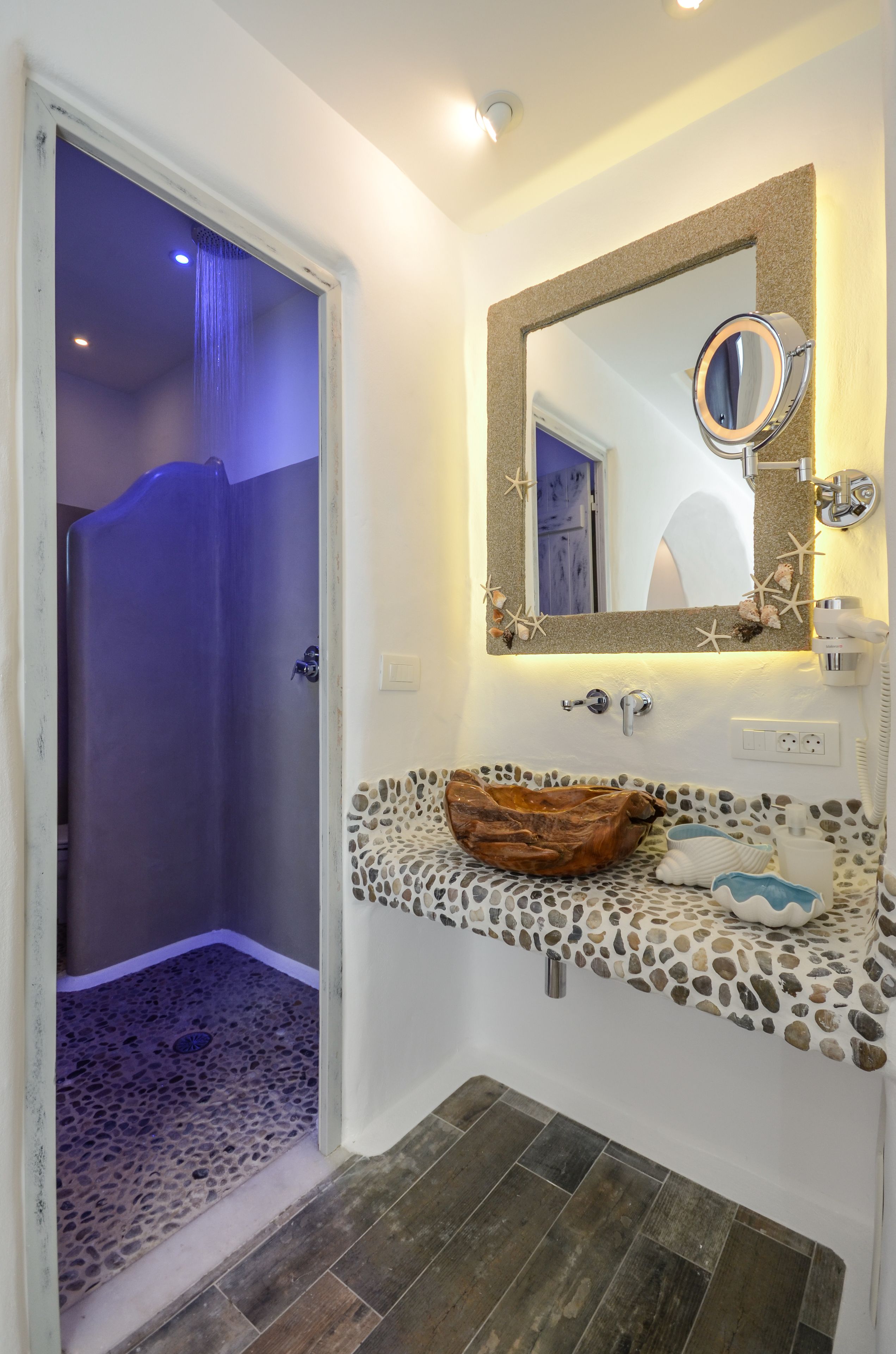A bathroom with a stone mosaic sink, a mirror with starfish decorations, and a shower with blue lighting.