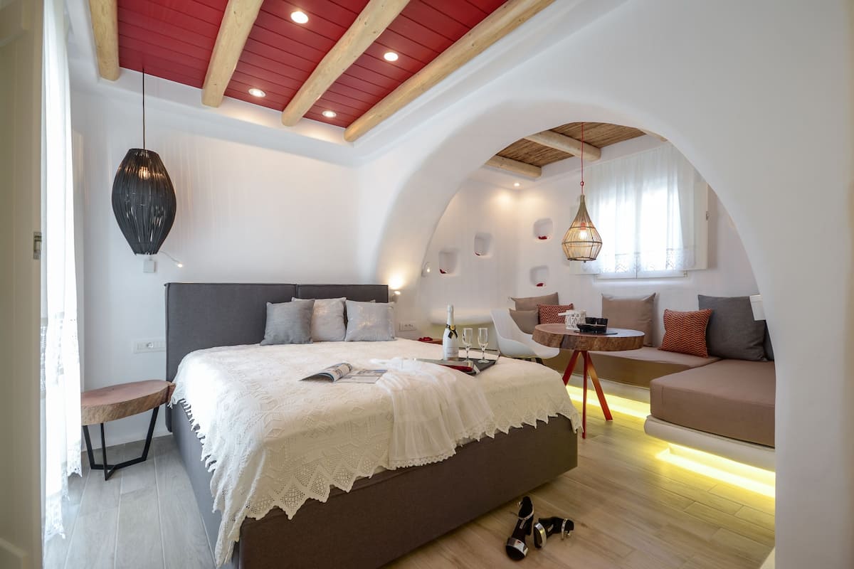 A bedroom with a large bed, a small table with a bottle and glasses, a bench, and a sofa.