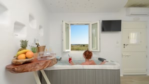 Una habitación con bañera, una mesa de madera con frutas y una bebida, y vistas al exterior.