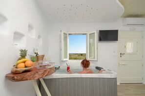 A room with a bathtub, a wooden table with fruits and a drink, and a view of the outdoors. - Naxos Island Escape (Naxos)