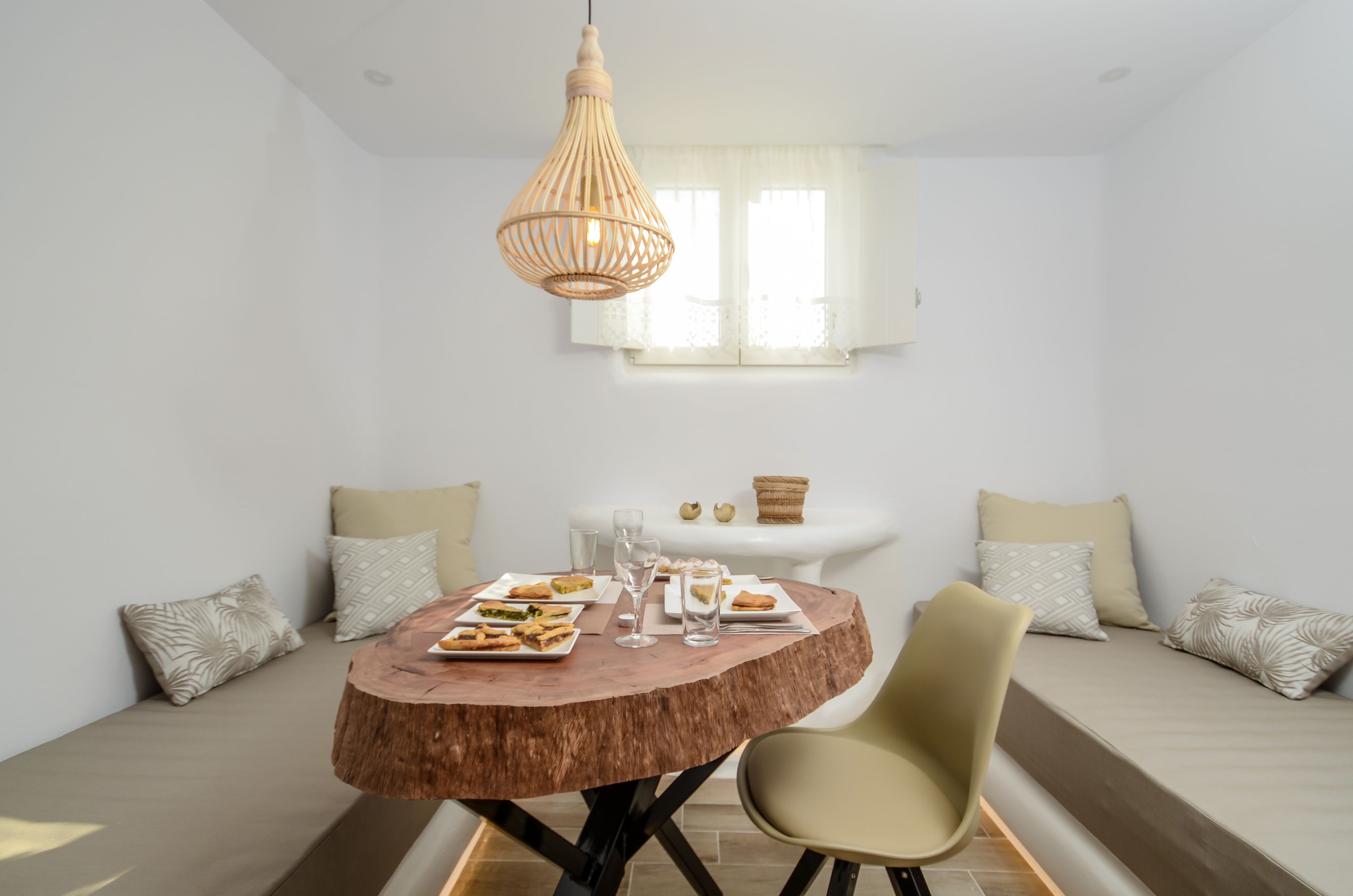 A dining area with a round wooden table, a hanging light fixture, and a sofa with cushions.