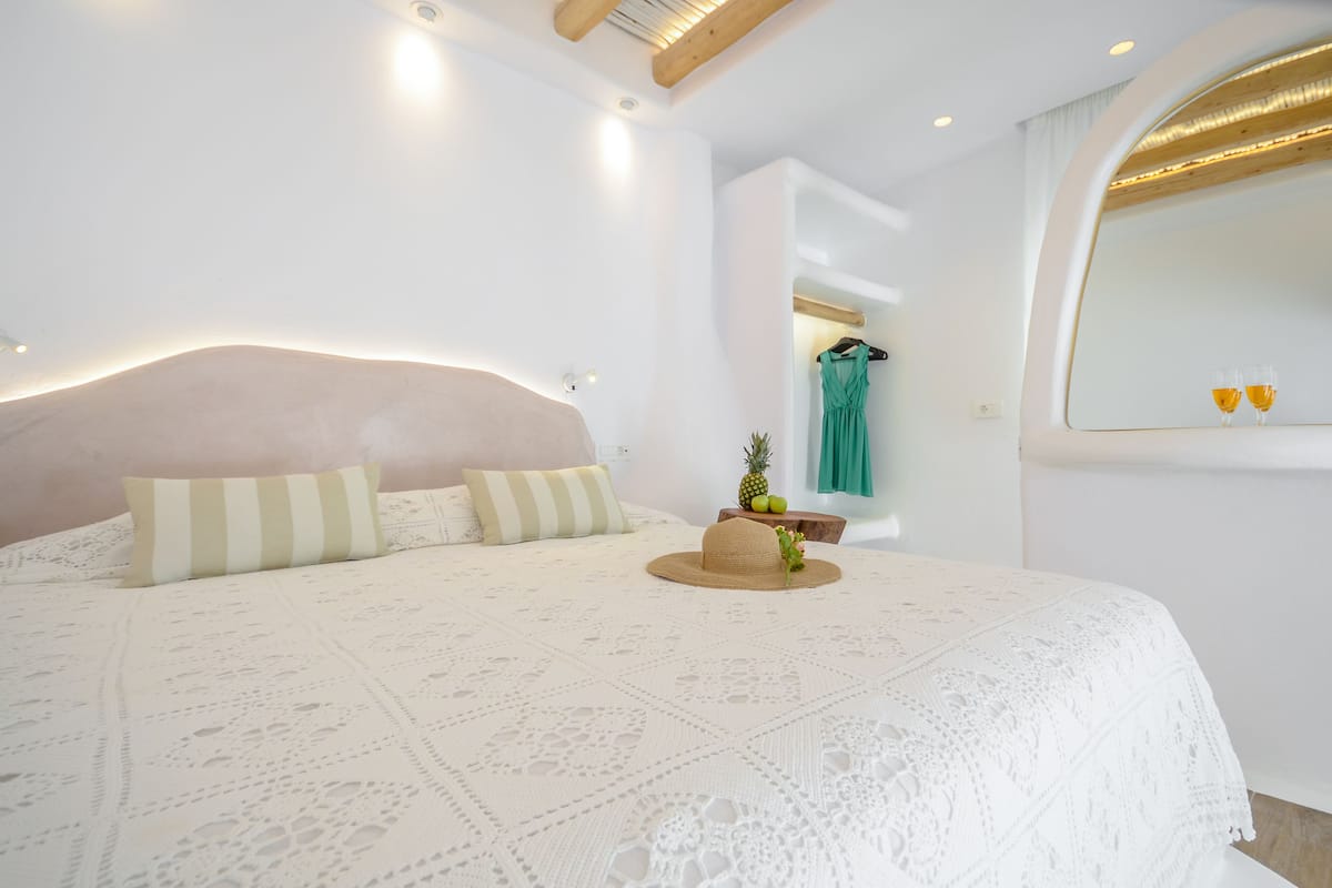 A neatly made bed with a white lace cover, a wooden headboard, and a straw hat with a pineapple on it.