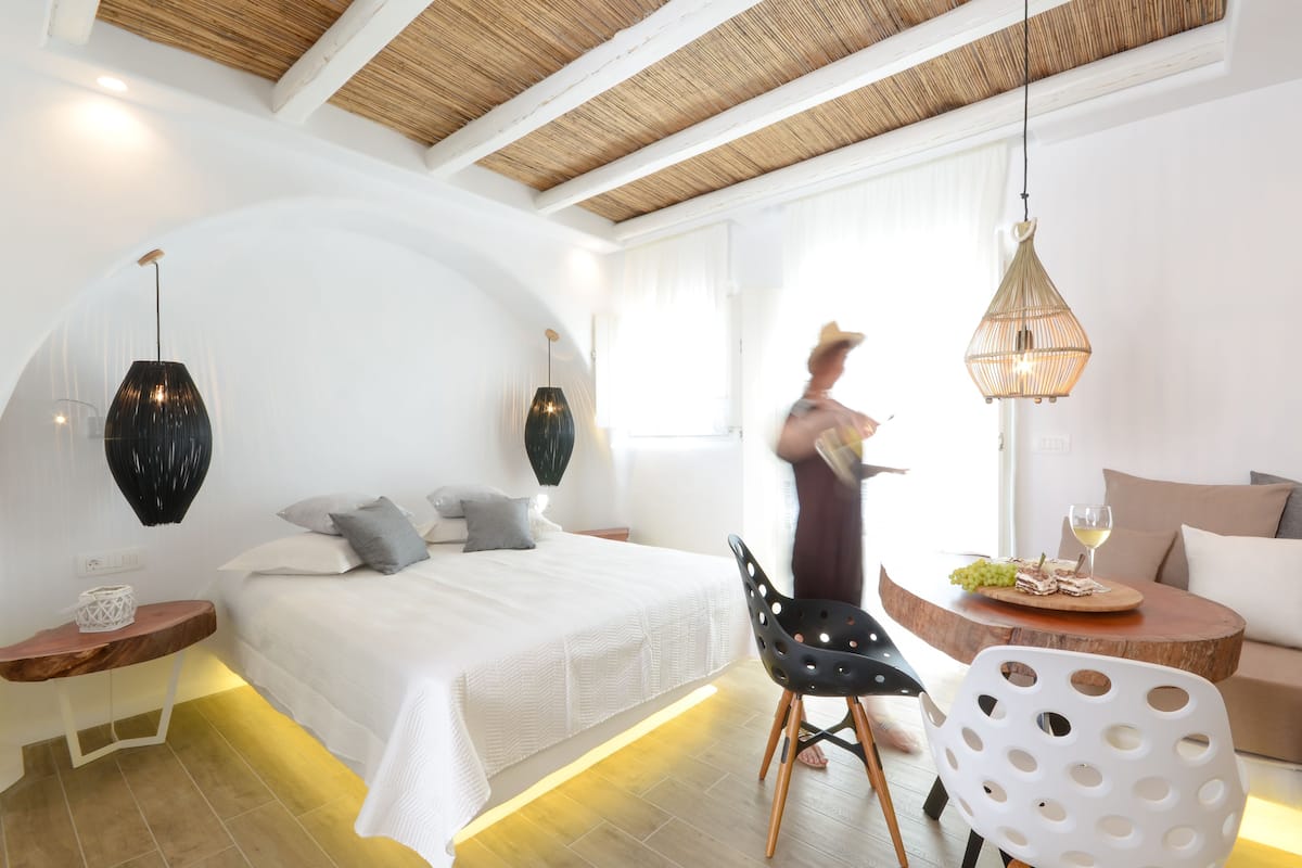A modern bedroom with a large bed, a wooden coffee table with a glass of wine and grapes, and a white chair.
