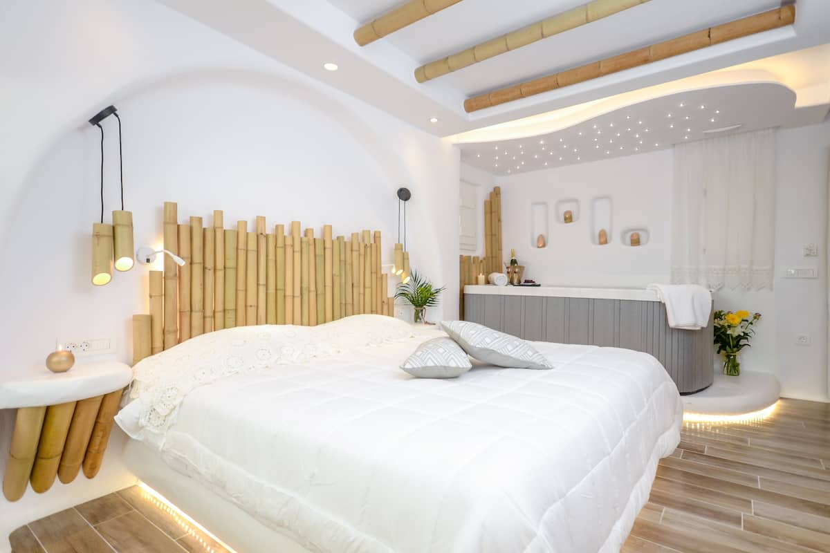 A modern bedroom with a large bed, a bedside table, a wall-mounted light, and a bathroom visible through an archway.