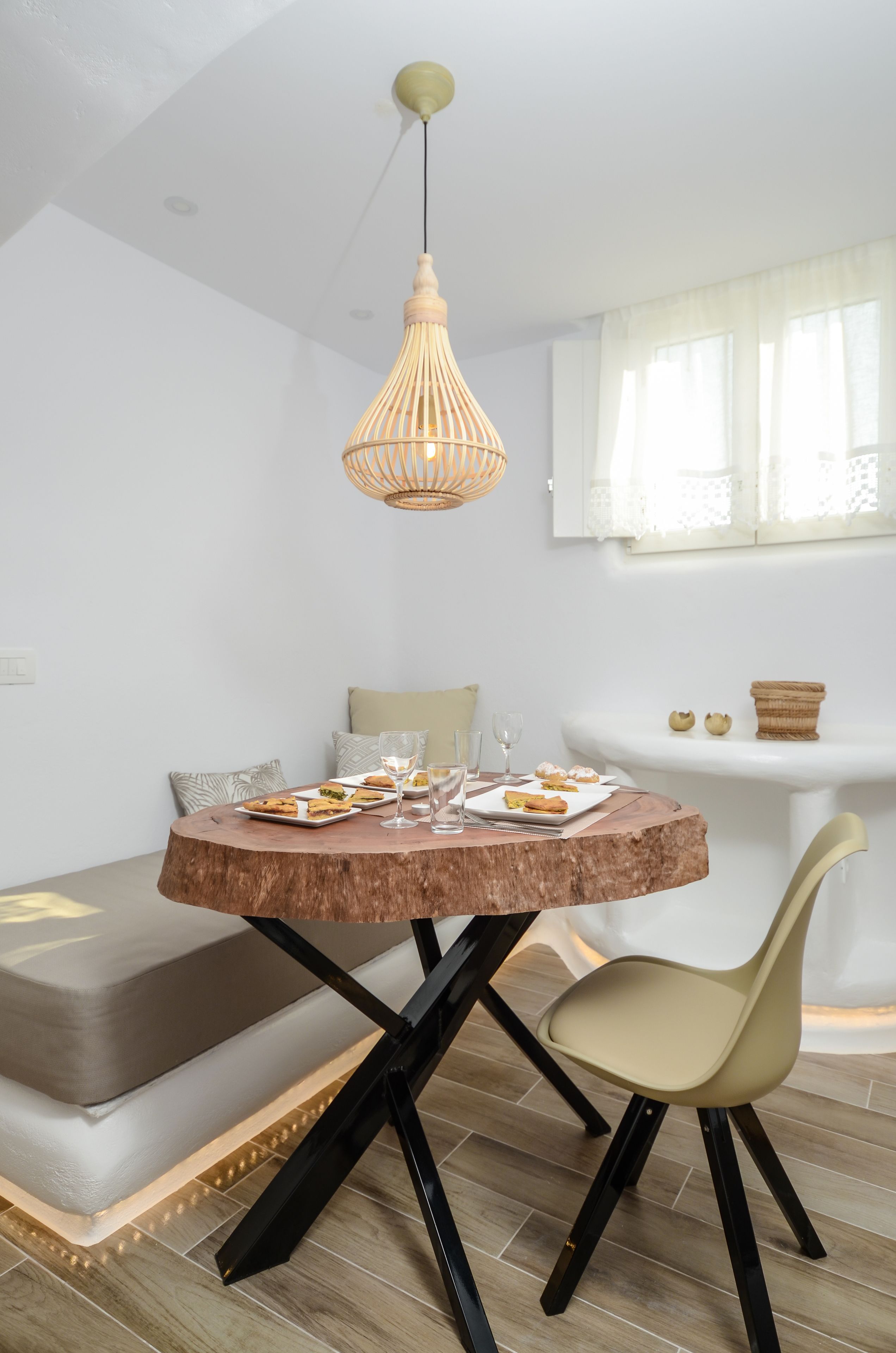 A dining area with a round wooden table, a beige chair, and a hanging light fixture.