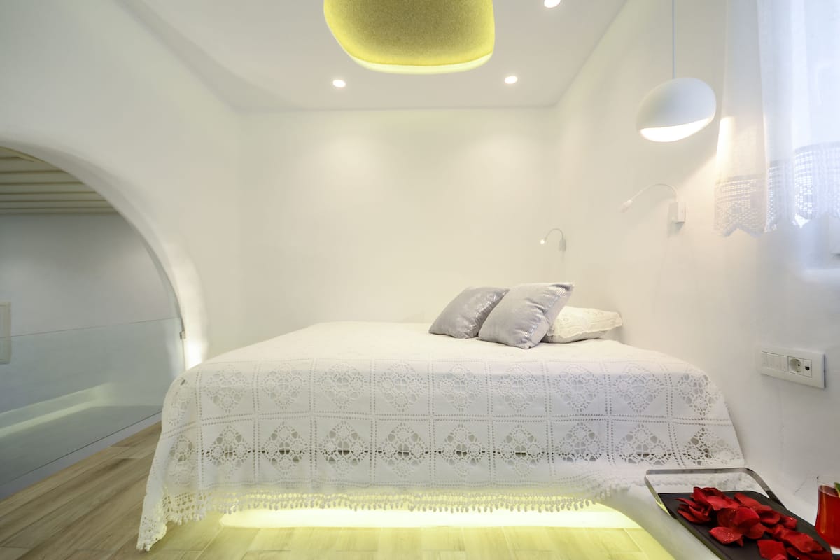 A modern bedroom with a white bed, a small bedside table, and a light fixture above the bed.