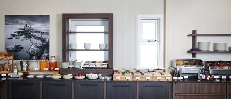 Een ontbijtbuffet met diverse etenswaren en toevoegingen, een groot raam en een lijst met kunstwerk aan de muur.