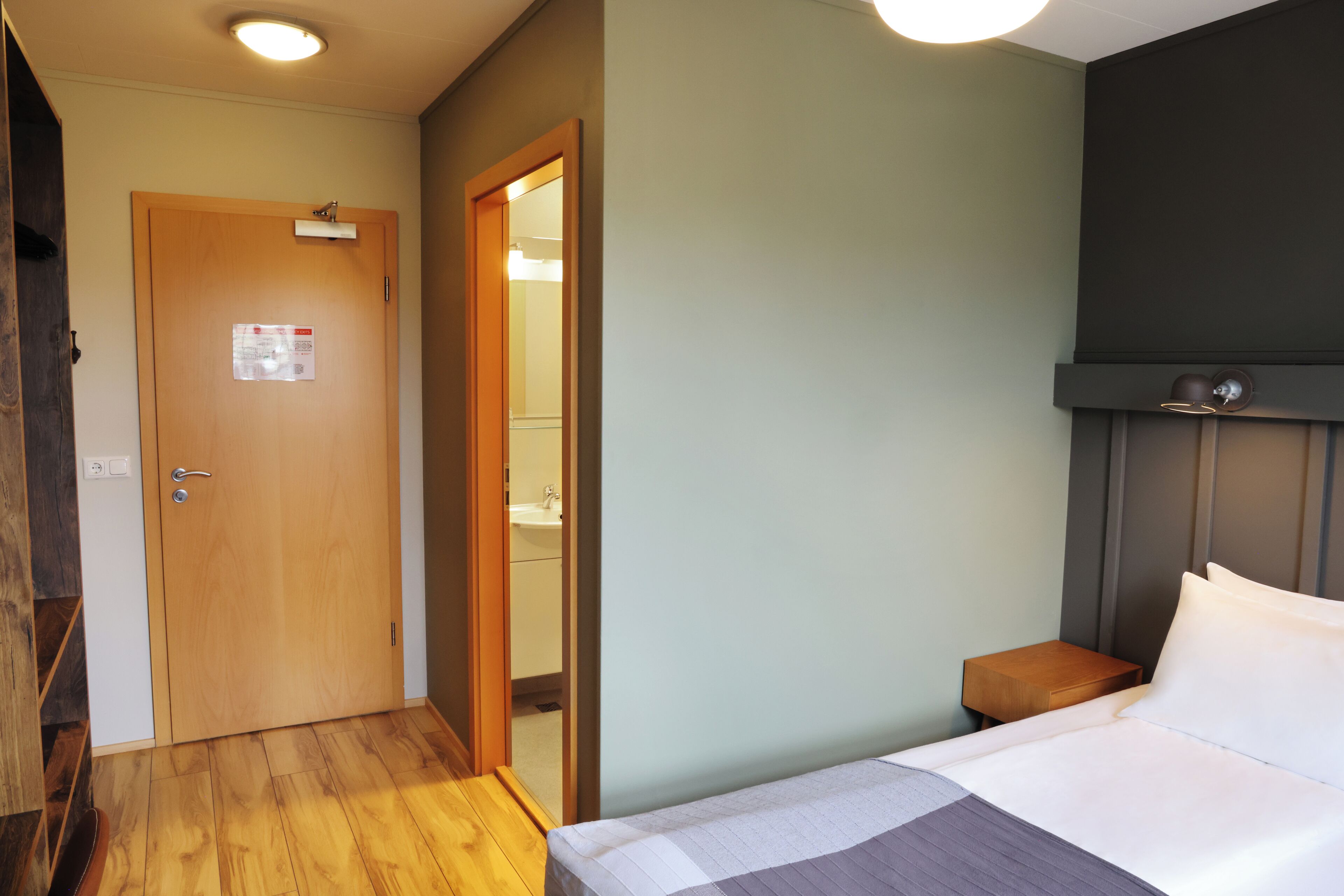 A bedroom with a wooden door, a bedside table, and a bed with white bedding.