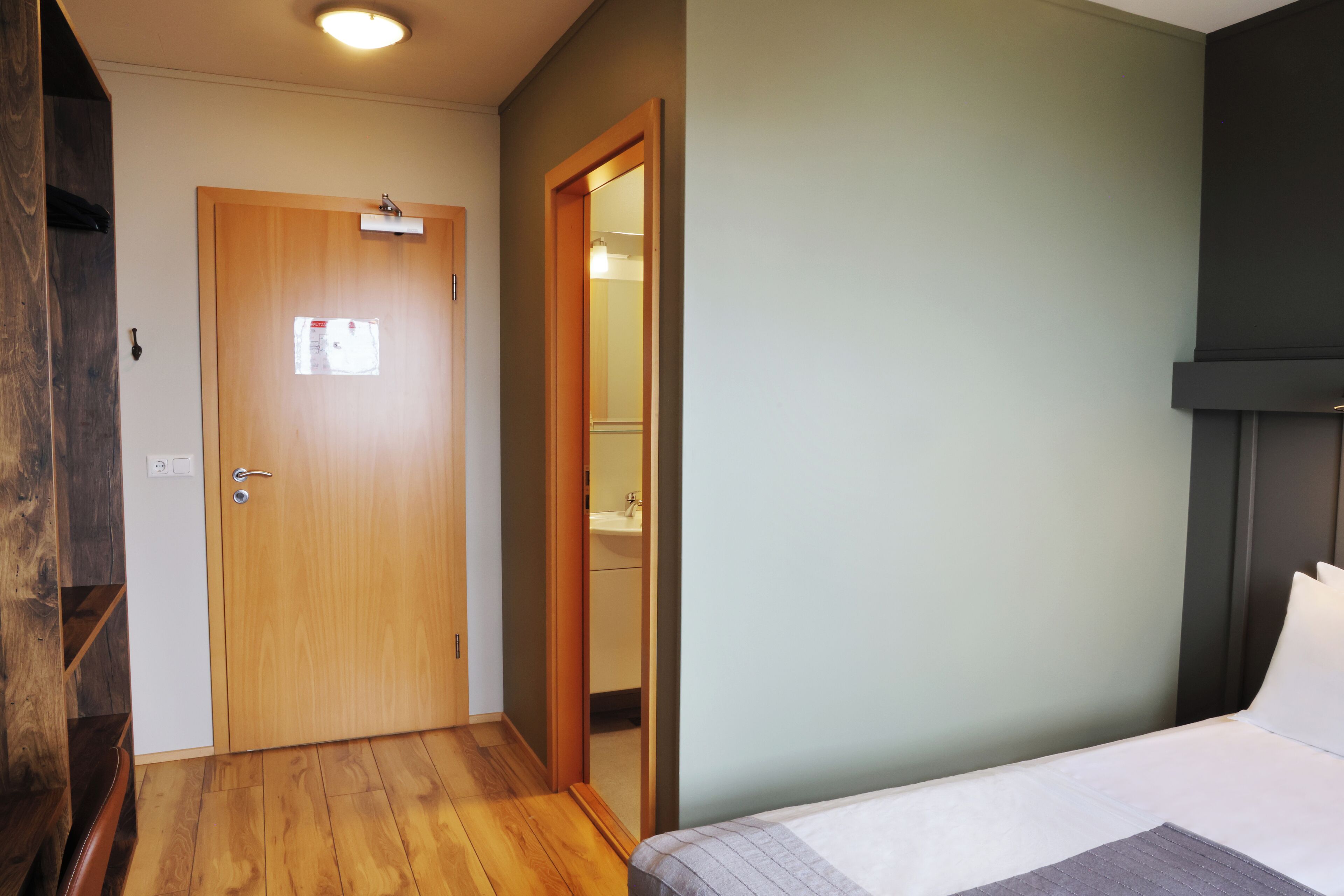 A hotel room with a wooden door, a visible bathroom, and a bed with a gray blanket.
