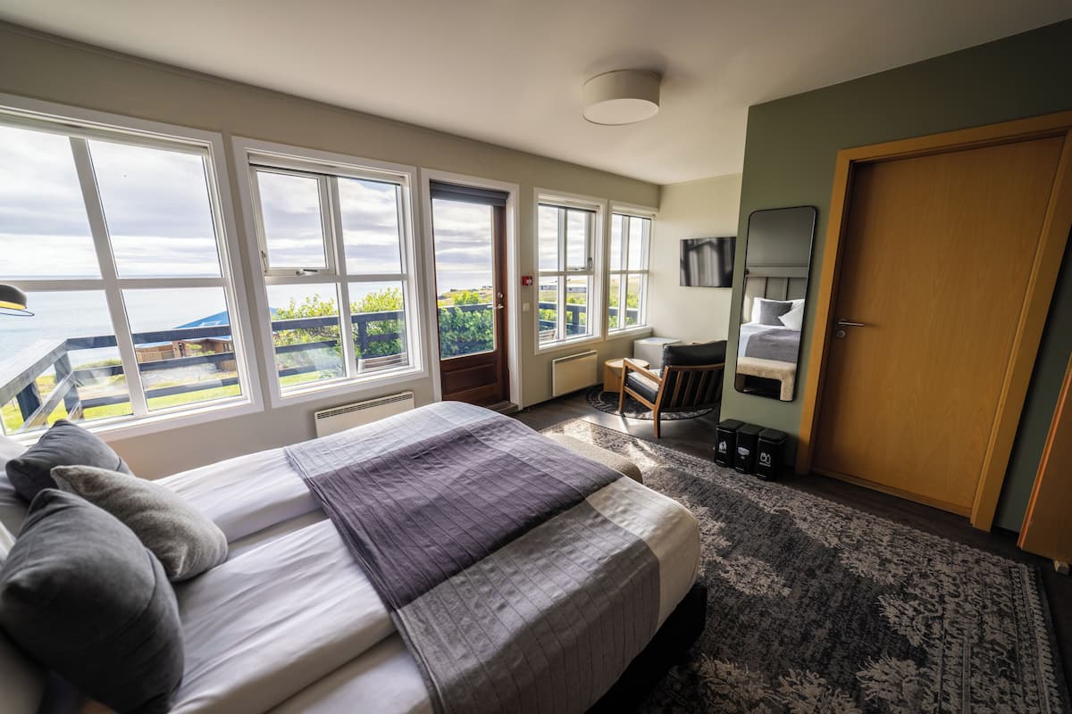 Ein Schlafzimmer mit einem großen Bett, einem Schreibtisch, einem Stuhl und Meerblick durch große Fenster.