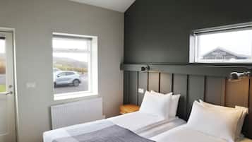 Un dormitorio con dos camas, una ventana que ofrece vistas a un coche y montañas, y un cabecero de color oscuro.