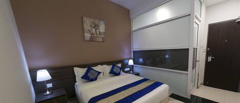A hotel room with a large bed, two bedside tables with lamps, a window with blinds, a door, and a painting on the wall.