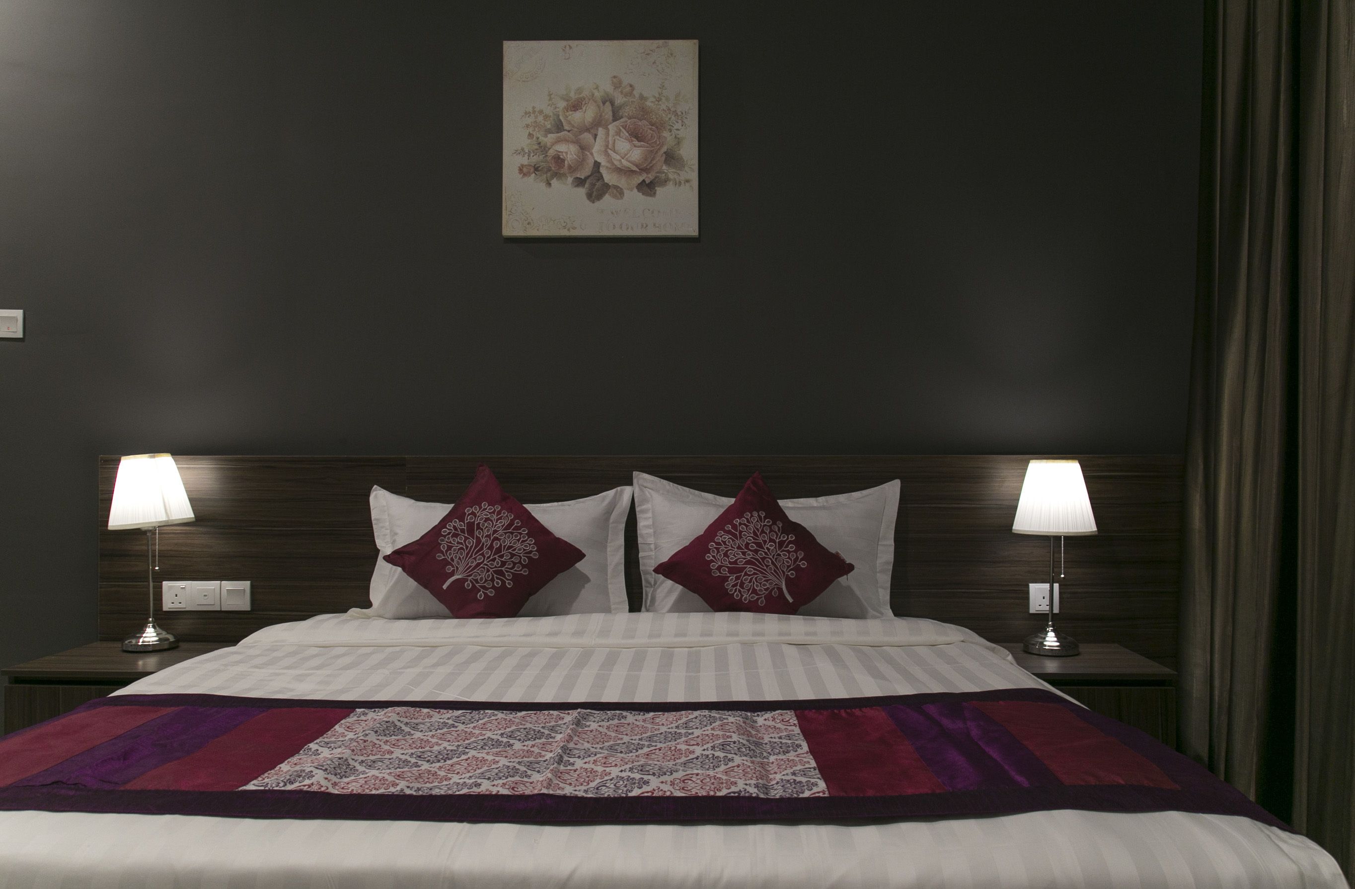 Una cama bien tendida con una colcha estampada, dos lámparas de noche y una obra de arte floral en la pared.